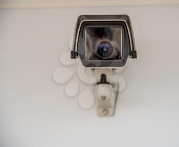 Front view of white video security camera mounted on wall and looking direct at viewer