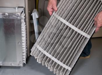 Senior caucasian man examining a folded dirty air filter in the HVAC furnace system in basement of home
