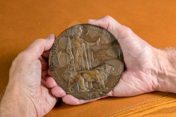 Hand holding historic memorial plaque or remembrance medal created in 1917 for British Soldiers who died in the Great War