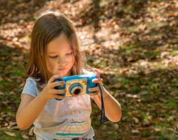 Small caucasian girl in a forest checking her photo on the back of a toy digital camera in concentration