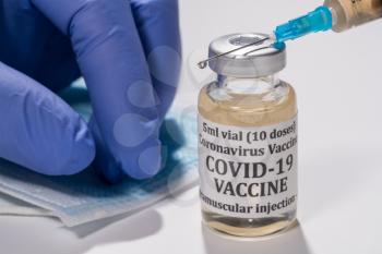 Covid-19 coronavirus vaccine with hypodermic syringe needle with droplet of liquid on tip. Gloved hand in background