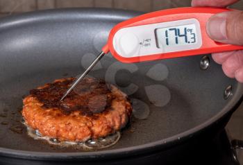 Charred and ready to eat plant-based burger in frying pan with instant thermometer confirming interior temperature