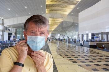 Senior man or traveler adjusting face mask in airport terminal and looking afraid of travel with coronavirus