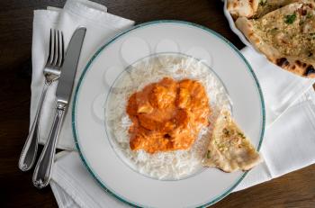 Chicken Tikka Masala with garlic Naan bread plated on white plate on napkin and taken from above