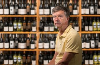 Senior old man looking at camera with a background of a wine cellar full of thousands of bottles on shelves