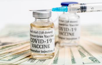 Covid-19 coronavirus vaccine with hypodermic syringe needle sitting on pile of cash to suggest payment for early vaccination