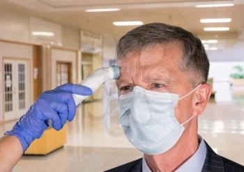 Mockup of hospital, clinic or shopping mall with senior adult wearing mask having a fever or temperature test taken to check coronavirus status