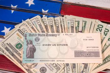 Stack of 20 dollar bills with illustrative coronavirus stimulus payment check on USA flag