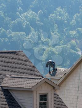 Young roofing contractor replacing the old shingles on a townhouse roof high above the ground