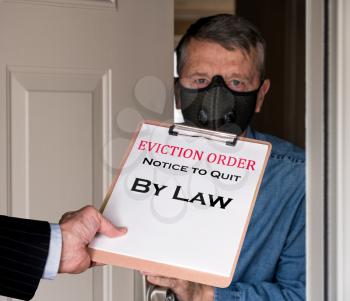 Open front door with man in suit handing an eviction notice to a defaulting renter with face mask during coronavirus epidemic