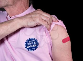Senior adult man showing his adhesive plaster over his covid-19 vaccination with sticker saying he got his vaccine