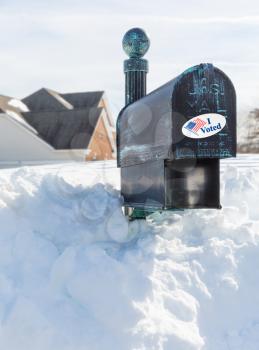 Metal mailbox for rural homes buried in deep snow with I Voted sticker as concept for voting by mail or absentee ballot paper