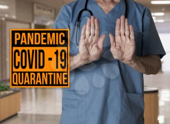 Doctor in blue scrups refusing entry to hospital with pandemic sign warning of quarantine due to Covid-19 or corona virus