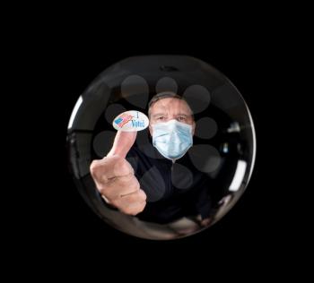 Senior man wearing face mask against virus and showing I voted sticker reflected inside fortune telling glass ball