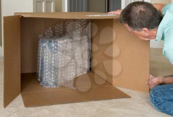 Senior man looking at a small boxed product surrounded by bubble wrap in a large almost empty delivery box in humorous photo