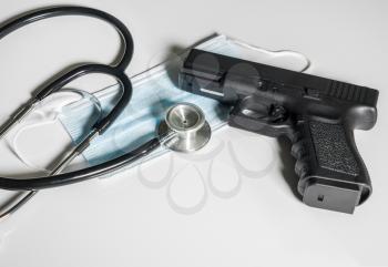 Pistol gun laying on top of medical mask in concept for dangers faced by front line medical personnel