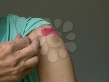 Senior caucasian man holding up shirt sleeve to show the bandaid after coronavirus vaccine shot in the shoulder