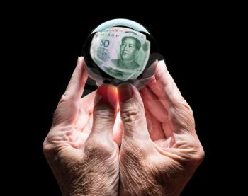 Senior caucasian hands holding a crystal futures or fortune ball reflecting a China 50 Yuan note as concept for the exchange rate for the currency
