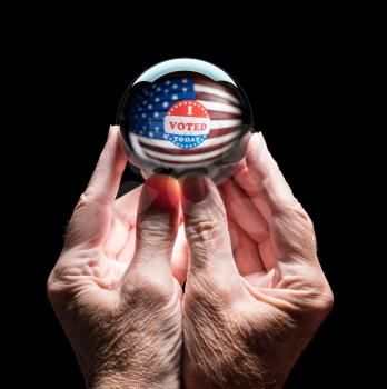Senior caucasian hands holding a crystal futures or fortune telling ball with I Voted sticker to predict the Presidential election results