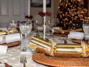 Traditional british christmas lunch table setting with crackers and glasses with xmas tree in the background
