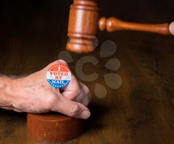 I voted by mail campaign sticker on senior hand under mallet and gavel. Illustrates the concept of judges overruling the rights of voters in election
