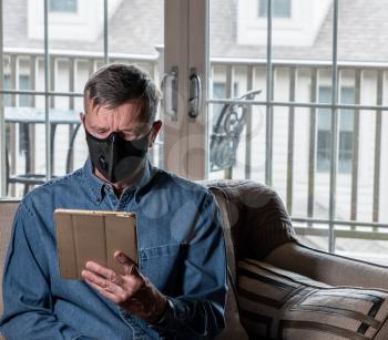 Concerned and worried man wearing a protective breathing mask against flu and coronavirus and reading news on tablet