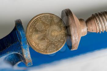 Concept for financial stress or recession with USA dollar coin being squeezed between the jaws of a large vise or vise in detailed macro shot