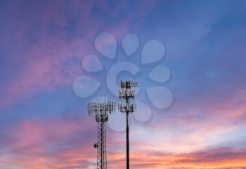 Two towers providing cellular broadband and data service to rural areas against the sunset. Illustrates digital divide.