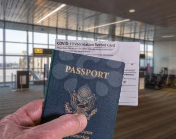 Mockup of airport terminal with businessman hand holding USA passport and vaccination certificate for coronavirus