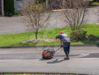 Worker compacting a layer of tarmac or extra blacktop to repair damage to asphalt street with a plate vibrator