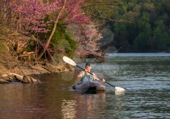 Caucasian man wearing PFD paddling towards the camera on a spring evening on a calm lake