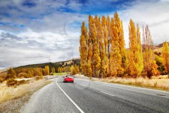 Autumn landscape with road and red car, New Zealand