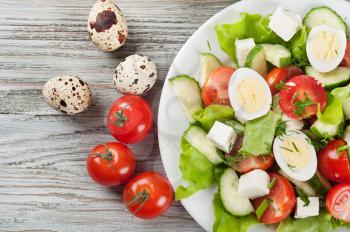 Fresh salad with quail eggs, cherry tomato, cucumber and lettuce on a wooden table. Top view.