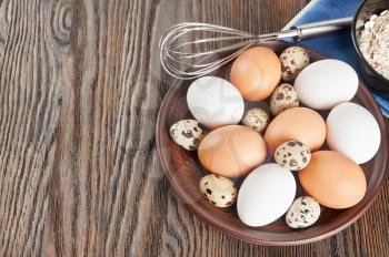 Quail and chicken eggs in a clay plate on a wooden background
