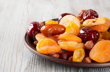 Dried fruits on a wooden background. Dates, lemon, apricots, figs and nuts in a clay plate.