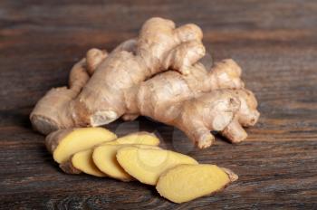 Fresh sliced ginger root on a dark brown wooden table. Healthy food and spices.