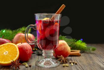 Mulled wine with spices and fruit on a wooden table on a black background. Traditional Christmas hot drink with red wine, apples, oranges and cinnamon