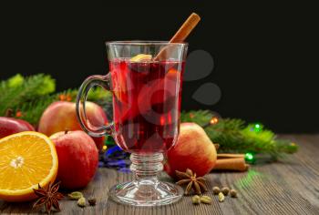 Mulled wine with spices and fruit on a wooden table on a black background. Traditional Christmas hot drink with red wine, apples, oranges and cinnamon
