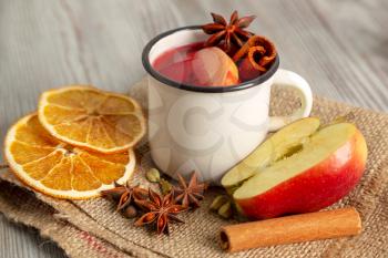 Mulled wine in white mug with fruit and spices on a wooden background. Traditional Christmas hot drink with red wine, apples, oranges, anise and cinnamon.