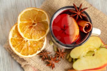 Mulled wine in white mug with fruit and spices on a wooden background. Traditional Christmas hot drink with red wine, apples, oranges, anise and cinnamon. Top view