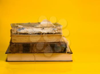 A stack of old shabby books with torn covers on a bright yellow background