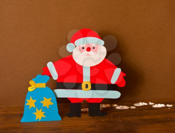 funny paper Santa Claus with bag of gifts in bright holiday clothes