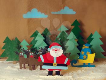 Funny Santa cut from colored cardboard with reindeer and sleigh with gifts in the forest