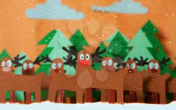 Team Reindeer Santa Claus standing in snowy forest. In front of red nosed Rudolph. The whole picture is cutting out from colored paper