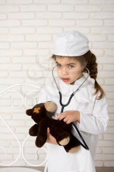 Little girl doctor in the white uniform with stethoscope and sick bear