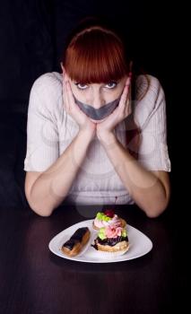 The girl, whose mouth sealed with tape sad looking at plate with cakes