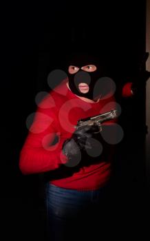 gangster with a pistol in mask on the face sneaks into the dark