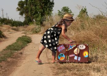 Little girl with suitcase in which the stickers from various countries waiting at the road passing trucks to get hitchhiking