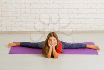 A little girl in a bright room on a gym mat rides and sports a twine