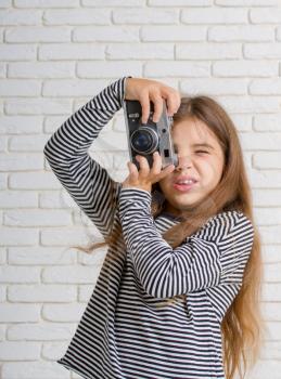 little girl in a striped blouse with a retro camera photographing standing near a light brick wall